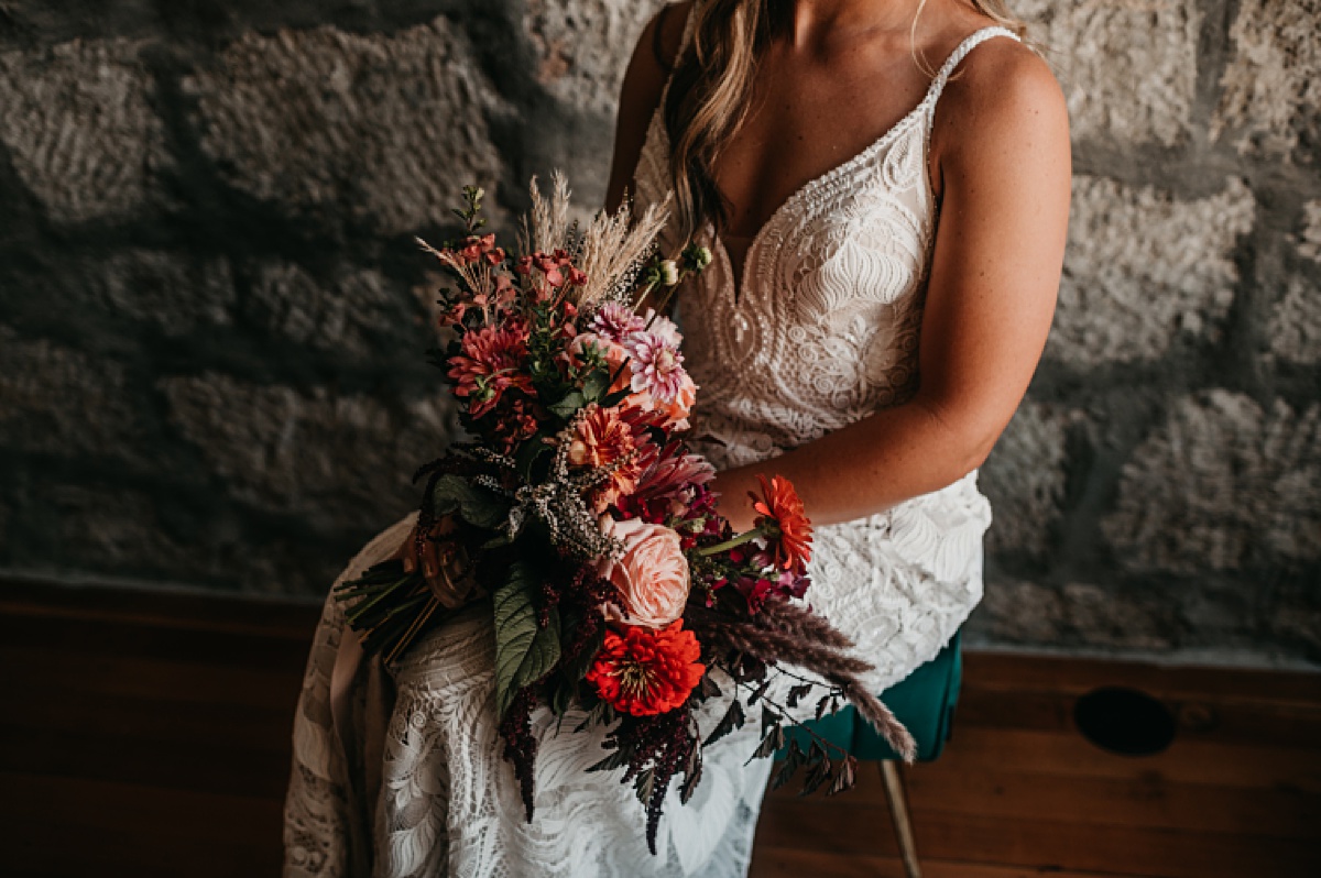 Boho bride is wearing an all lace wedding dress, loose boho waves in her hair, and a vibrant moody wedding bouquet. 