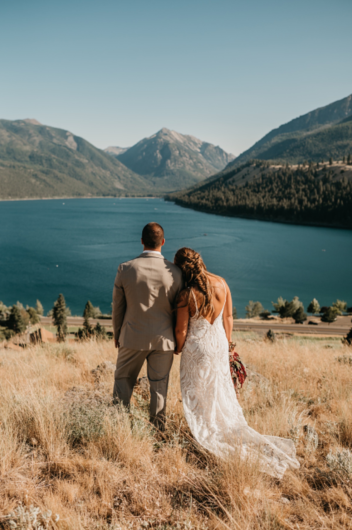 Bride and groom are standing above Wallowa Lake in Joseph Oregon at sunset taking in the view.