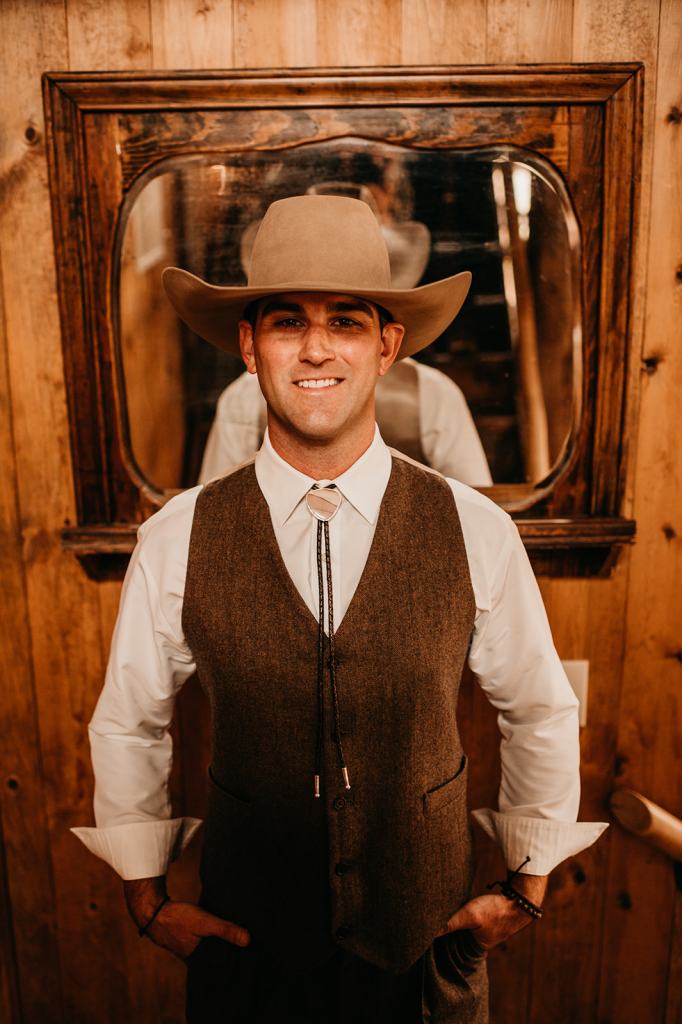Groom wearing a cowboy hat and bolo tie gets ready before his wedding day in Steamboat Springs Colorado