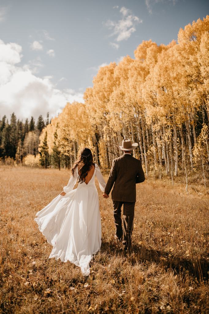 Bride and groom walk among forest of yellow and orange aspens on their elopement day in Steamboat Springs Colorado