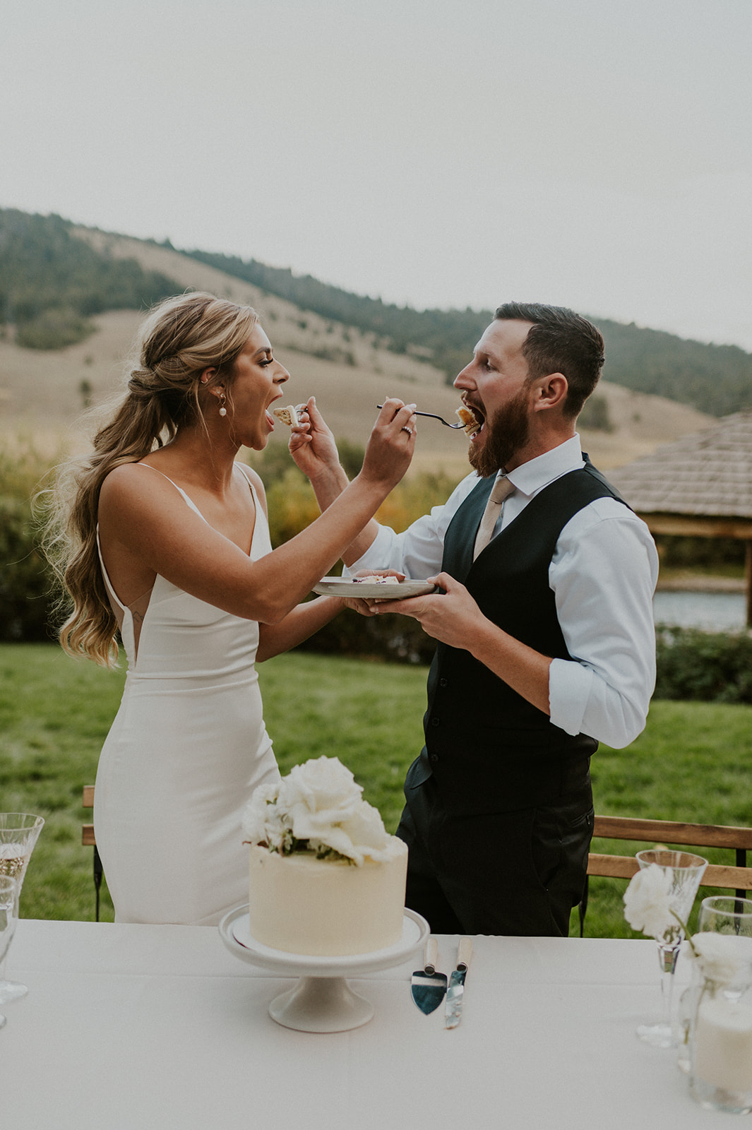Bride and groom laugh as they cut their wedding cake in Stanley Idaho