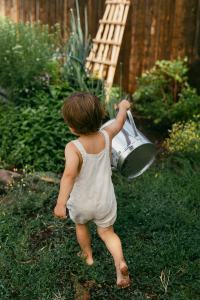 Toddler running through the garden with a water can